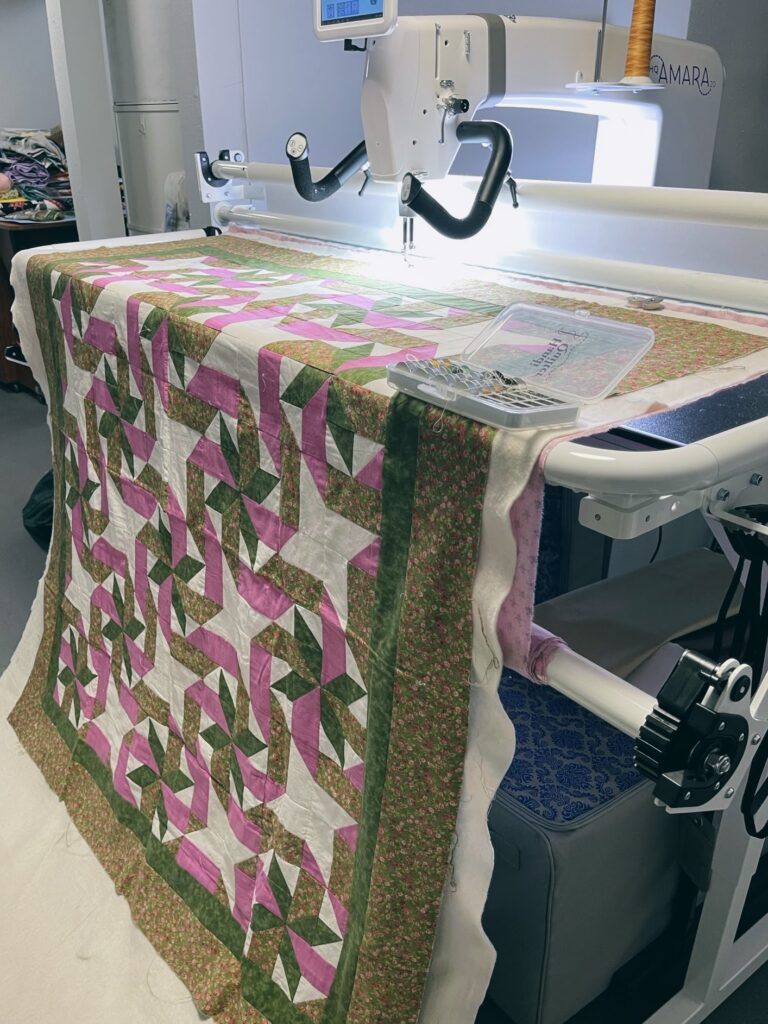 An 8-point star quilt motif with a ribbon pattern connecting the stars - pink, green, and white - loaded onto a long-arm machine