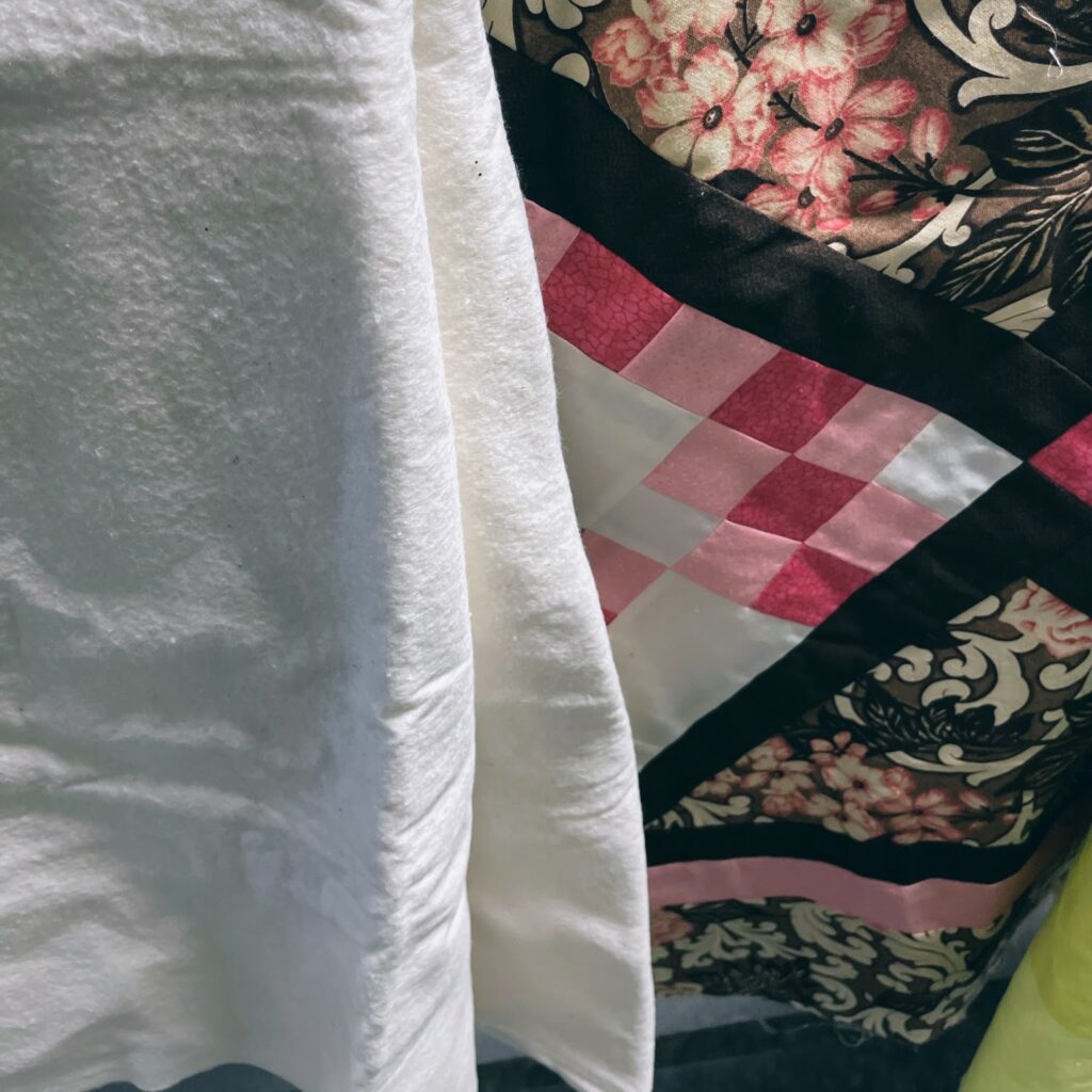 White quilt batting layered on top of a pink and brown quilt